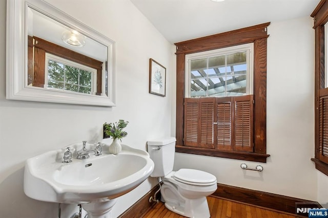 half bath featuring baseboards, a sink, toilet, and wood finished floors