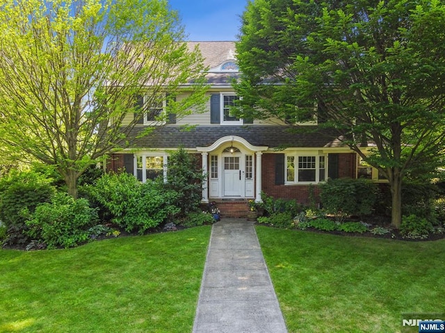 view of front facade with a shingled roof, brick siding, and a front lawn