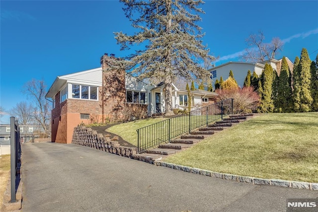 view of front facade featuring a chimney, fence, a front lawn, and brick siding