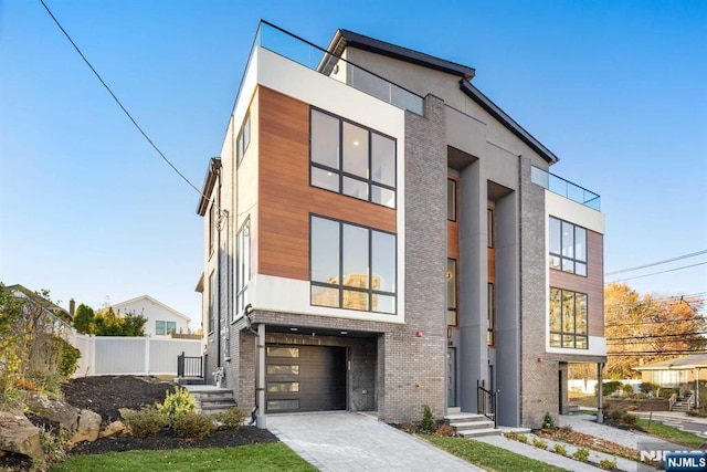 modern home featuring driveway, brick siding, an attached garage, and fence