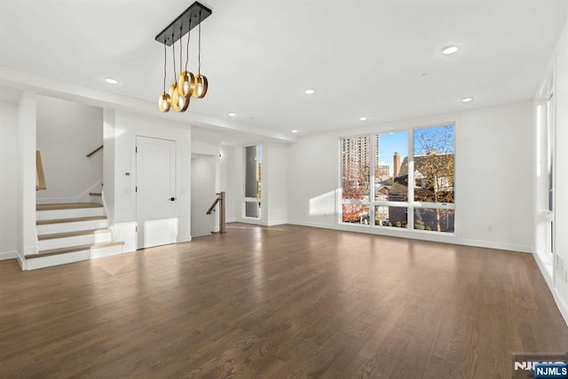 unfurnished living room featuring recessed lighting, a notable chandelier, baseboards, and wood finished floors