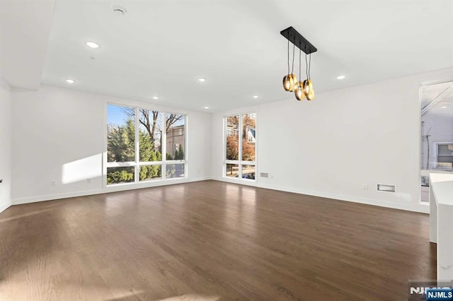 unfurnished living room featuring a notable chandelier, baseboards, dark wood-type flooring, and recessed lighting