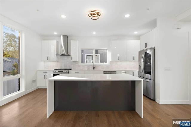 kitchen featuring light countertops, appliances with stainless steel finishes, a sink, a kitchen island, and wall chimney exhaust hood