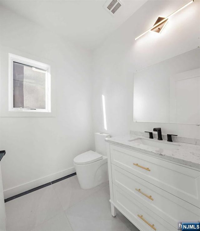 half bath with toilet, vanity, visible vents, and baseboards