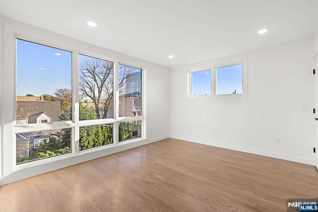 unfurnished room featuring a healthy amount of sunlight, baseboards, wood finished floors, and recessed lighting