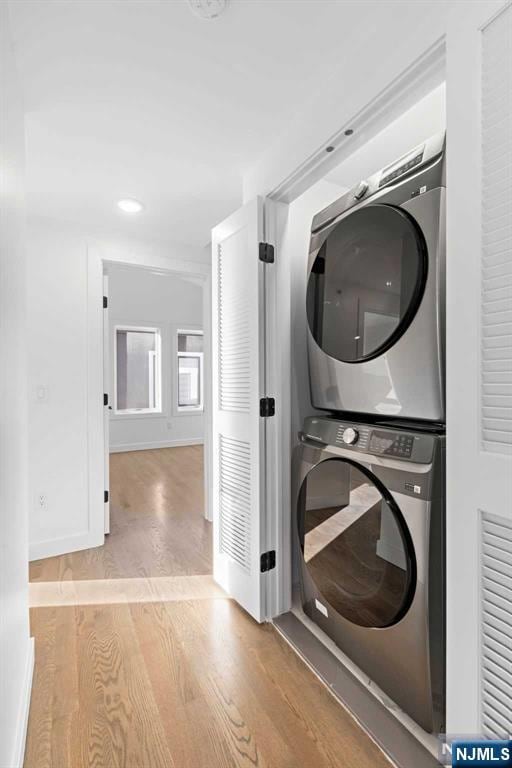 laundry area featuring baseboards, laundry area, wood finished floors, and stacked washer / drying machine