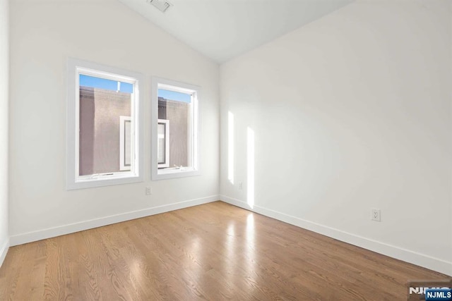 unfurnished room with visible vents, vaulted ceiling, baseboards, and wood finished floors