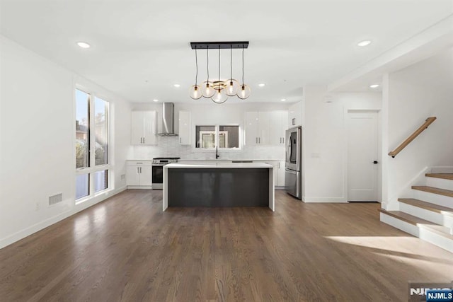 kitchen with wall chimney exhaust hood, a kitchen island, stainless steel appliances, white cabinetry, and backsplash