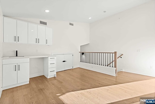 unfurnished office with light wood-type flooring, a sink, and visible vents