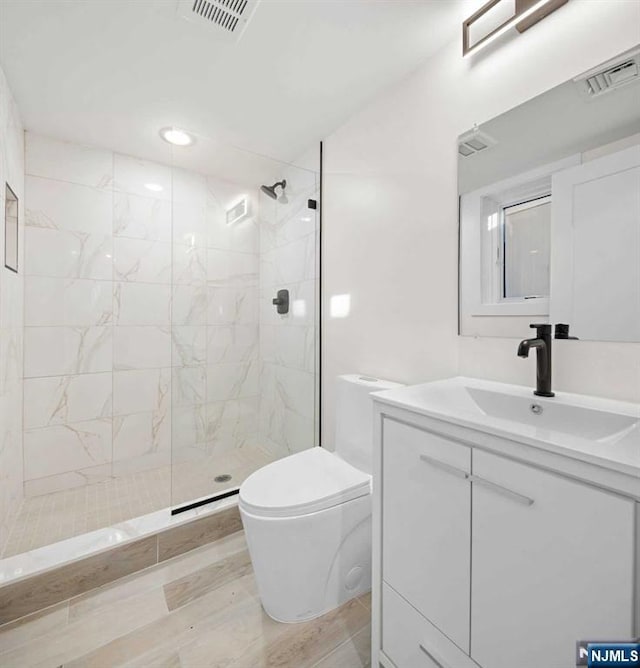 bathroom with visible vents, tiled shower, wood finished floors, and toilet