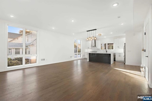 unfurnished living room with an inviting chandelier, baseboards, dark wood finished floors, and recessed lighting