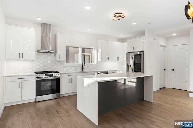 kitchen featuring modern cabinets, appliances with stainless steel finishes, wall chimney range hood, white cabinetry, and a sink