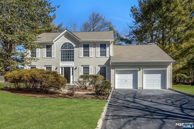 colonial house featuring driveway, a front lawn, roof with shingles, and an attached garage