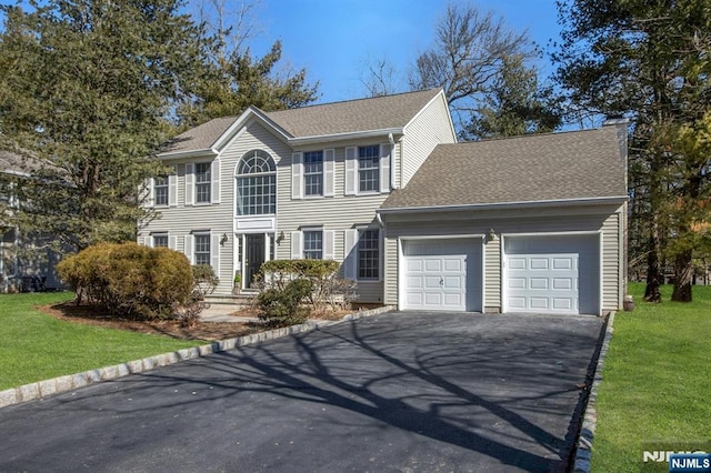 colonial-style house featuring a front lawn, driveway, a shingled roof, and an attached garage