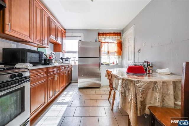 kitchen featuring brown cabinets, freestanding refrigerator, gas range oven, light countertops, and black microwave