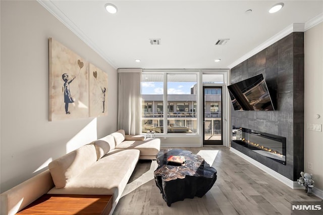 living room featuring visible vents, crown molding, a fireplace, and wood finished floors