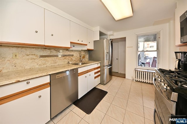 kitchen featuring stainless steel appliances, radiator heating unit, white cabinetry, and decorative backsplash