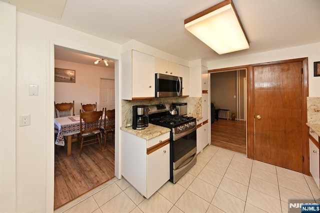 kitchen with light tile patterned floors, white cabinets, appliances with stainless steel finishes, decorative backsplash, and radiator