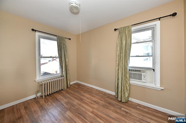 unfurnished room featuring cooling unit, baseboards, radiator heating unit, and wood finished floors