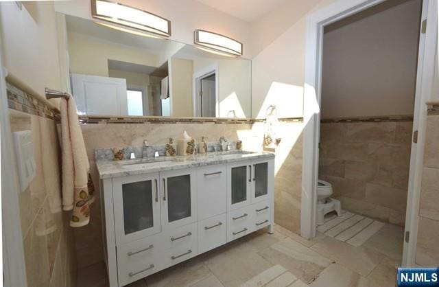 bathroom with a sink, tile walls, toilet, and double vanity