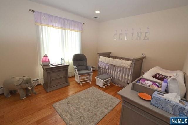 bedroom with a crib, visible vents, light wood-style floors, a baseboard heating unit, and recessed lighting