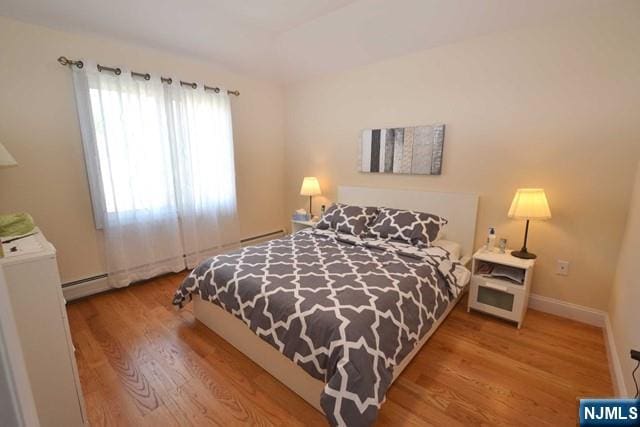 bedroom with a baseboard radiator, baseboards, and wood finished floors