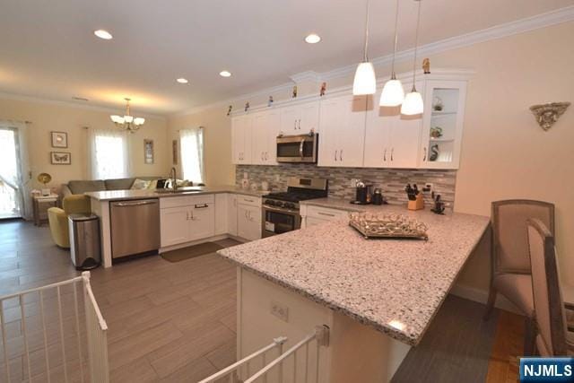 kitchen featuring decorative backsplash, appliances with stainless steel finishes, ornamental molding, white cabinets, and a peninsula