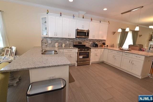 kitchen featuring a peninsula, a sink, white cabinets, appliances with stainless steel finishes, and crown molding