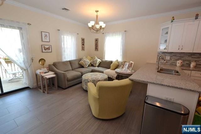 living area with an inviting chandelier, light wood-style flooring, visible vents, and ornamental molding