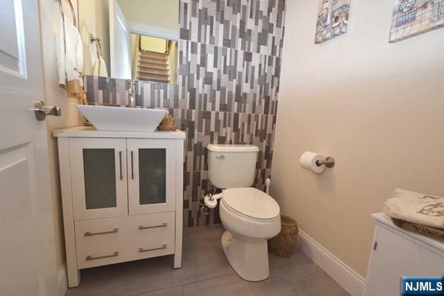 bathroom featuring tile patterned flooring, toilet, vanity, baseboards, and tile walls