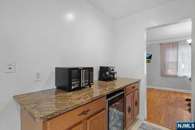 kitchen with stone counters, light wood-type flooring, beverage cooler, and brown cabinets