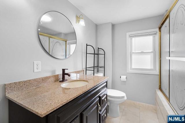 bathroom with toilet, combined bath / shower with glass door, vanity, and baseboards