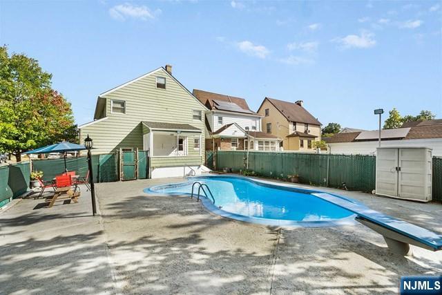 view of swimming pool featuring an outbuilding, a patio area, a shed, a fenced backyard, and a diving board