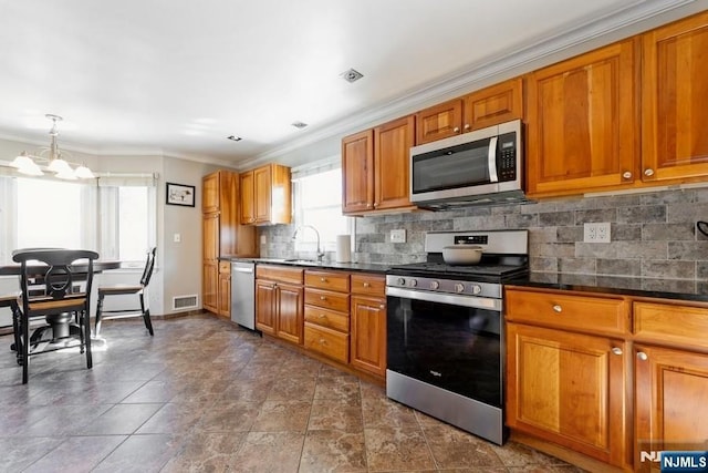 kitchen with stainless steel appliances, dark countertops, a sink, and brown cabinets