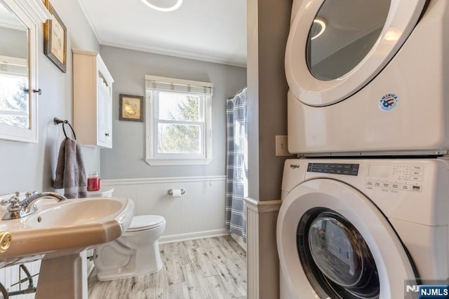 bathroom featuring crown molding, toilet, stacked washer / dryer, wainscoting, and wood finished floors