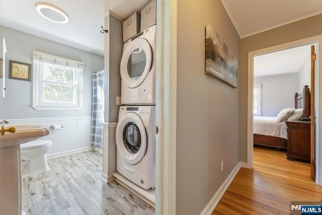 washroom featuring stacked washer and dryer, laundry area, a wainscoted wall, ornamental molding, and wood finished floors