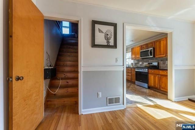 kitchen with brown cabinets, tasteful backsplash, visible vents, appliances with stainless steel finishes, and light wood-type flooring