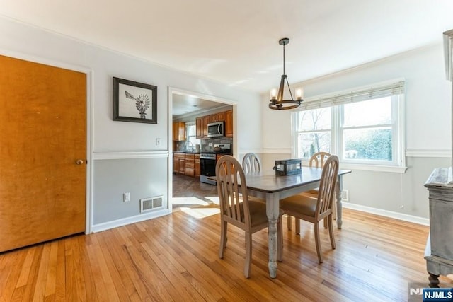 dining room with light wood finished floors, baseboards, visible vents, and an inviting chandelier