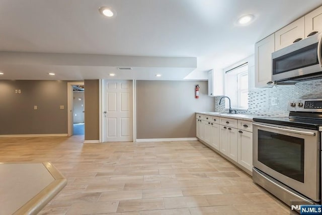 kitchen with a sink, baseboards, white cabinets, appliances with stainless steel finishes, and tasteful backsplash