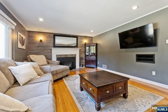 living room featuring a fireplace with flush hearth, visible vents, light wood-style flooring, and crown molding