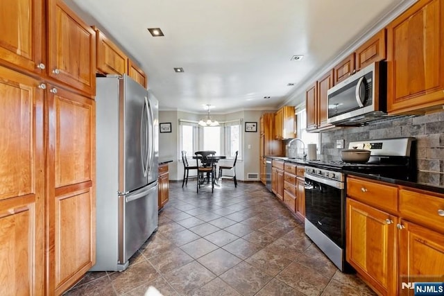 kitchen featuring brown cabinets, a notable chandelier, dark countertops, backsplash, and appliances with stainless steel finishes