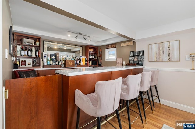 bar featuring rail lighting, a community bar, light wood-style floors, and baseboards