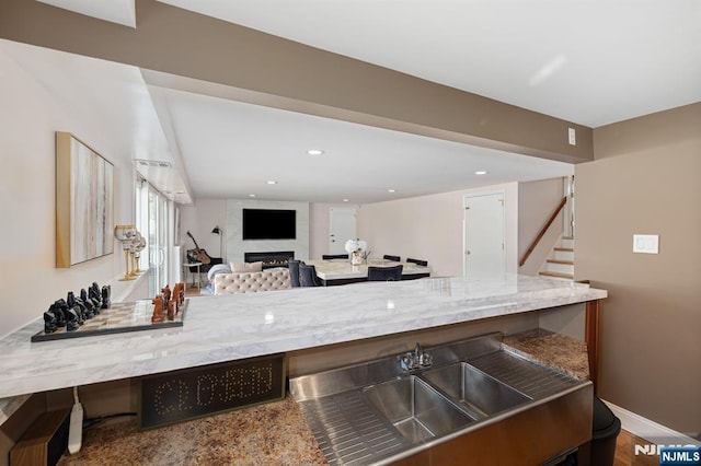 kitchen featuring light stone countertops, baseboards, recessed lighting, a fireplace, and a sink