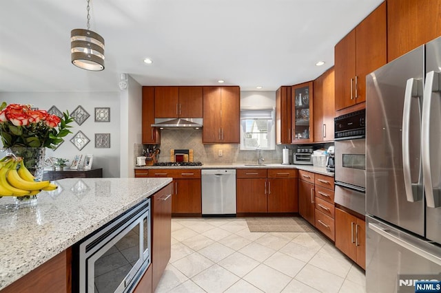 kitchen with a sink, under cabinet range hood, appliances with stainless steel finishes, a warming drawer, and tasteful backsplash