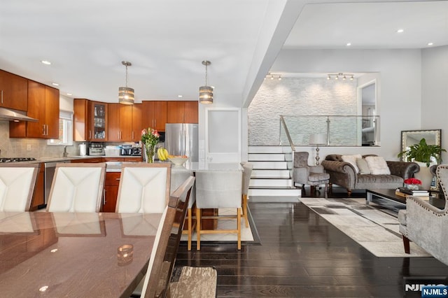 kitchen featuring stainless steel appliances, brown cabinets, tasteful backsplash, and dark wood finished floors