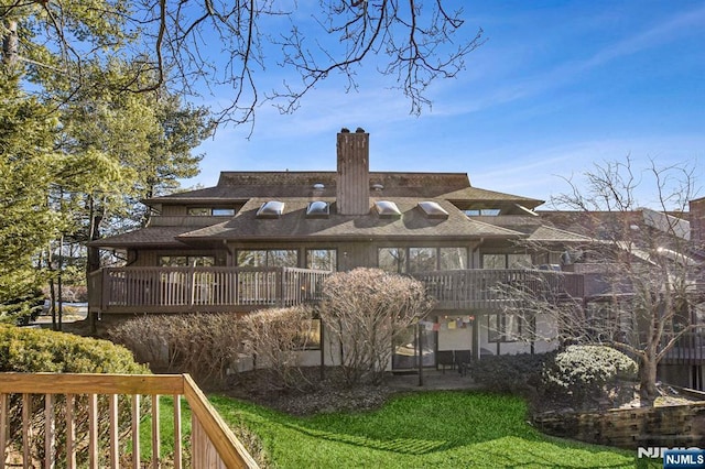 back of house featuring a deck, a lawn, a chimney, and a shingled roof