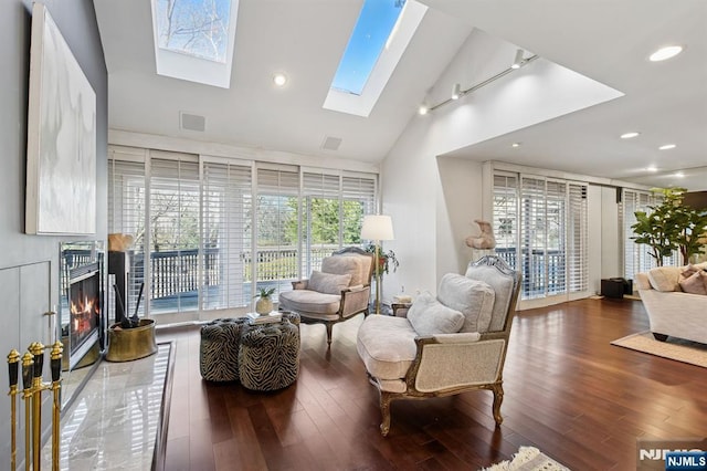 living area with high vaulted ceiling, a skylight, wood finished floors, visible vents, and a glass covered fireplace