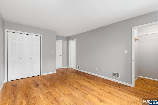 unfurnished bedroom featuring light wood-type flooring, baseboards, a closet, and visible vents