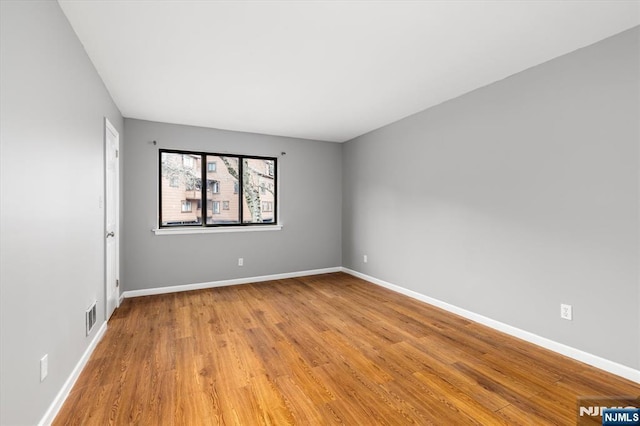 empty room with wood finished floors, baseboards, and visible vents