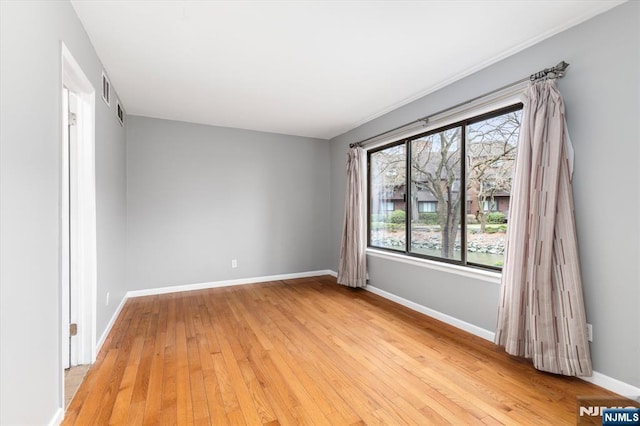 empty room featuring light wood finished floors, visible vents, and baseboards